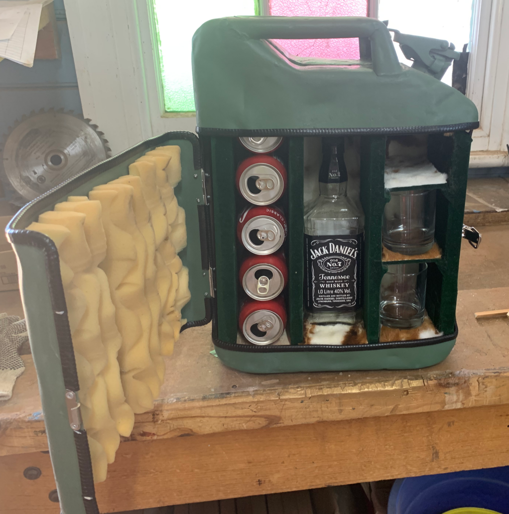 A portable bar made from a jerrycan with spaces for cans, a bottle of Jack Daniels and glasses